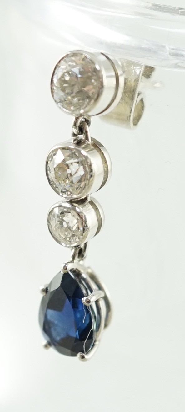 A pair of 1980's platinum, single stone pear cut sapphire and graduated three stone collet set diamond drop earrings